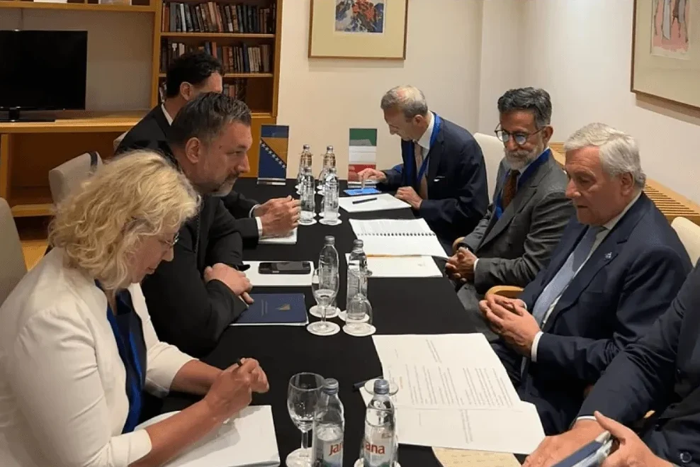 Grupa diplomata sjedi za stolom tokom sastanka, sa zastavama Bosne i Hercegovine i Italije vidljivim na stolu.