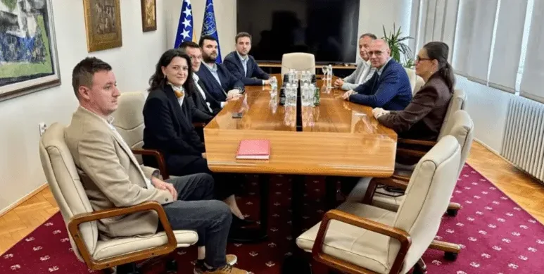 Grupa ljudi sjedi za velikim drvenim stolom u prostoriji, vjerovatno u ministarstvu ili vladinoj instituciji.