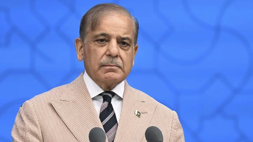 Portret premijera Pakistana, Shehbaza Sharifa, u bež prugastom odijelu, sa crnom kravatom sa bijelim i ružičastim prugama. Na reveru sakoa mu je mali pakistanski grb. Gospodin Sharif stoji ispred plave pozadine sa uzorkom i ima ozbiljan izraz lica.