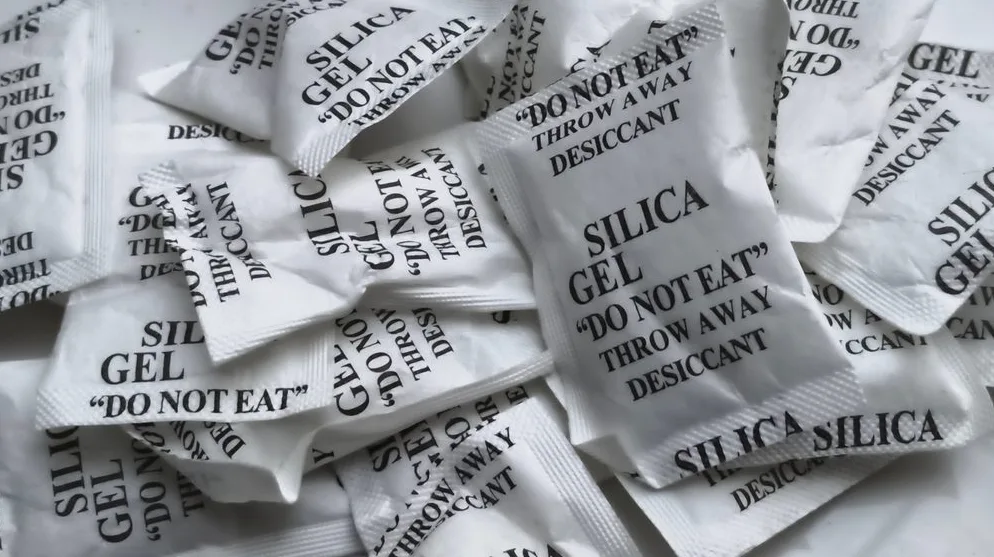 Puna gomila malih bijelih pakovanja sa natpisom "SILICA GEL" i "DO NOT EAT, THROW AWAY DESICCANT".