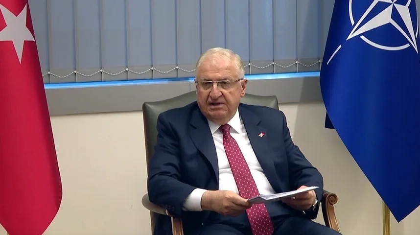 Političar u tamnom odijelu i crvenoj kravati, sjedi pored zastave Turske i zastave NATO-a.