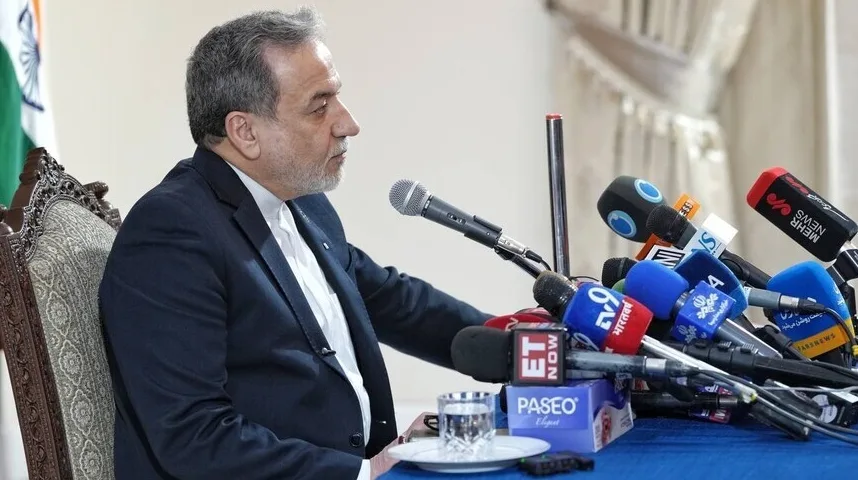 Političar u tamnom odijelu sjedi za stolom sa brojnim mikrofonima ispred sebe, sa zastavom Indije u pozadini.