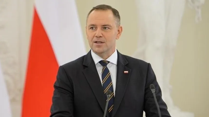 Poljski zvaničnik u tamnom odijelu i kravati, sa poljskom zastavom u pozadini.