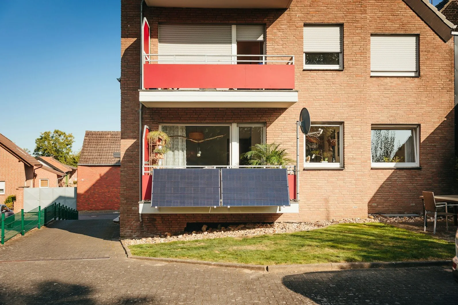 Stambena zgrada od crvene opeke s balkonima, na jednom su postavljena dva plava solarna panela.