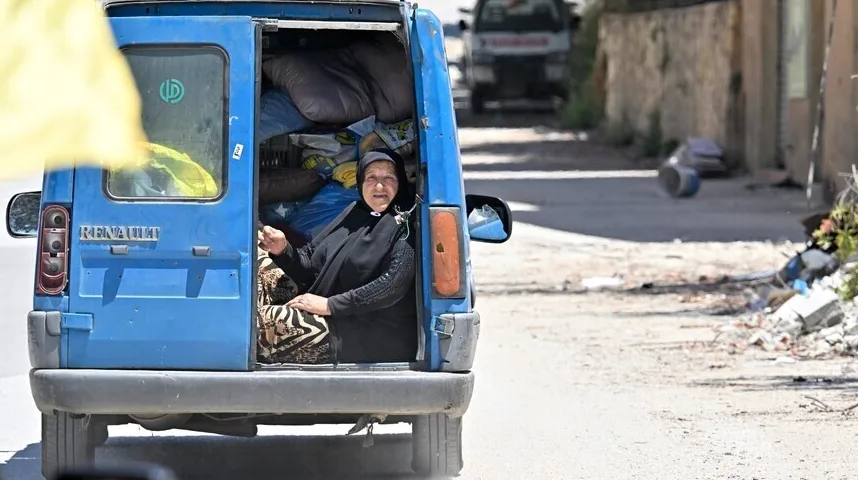 Starija žena u crnom hidžabu sjedi u zadnjem dijelu plavog Renault kombija natrpanog prtljagom.