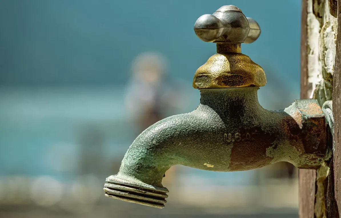 Detaljan prikaz starinske, zarđale i patinirane metalne slavine sa mesinganom ručkom i navojem za crijevo na drvenom stubu.
