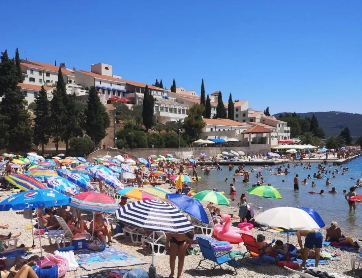 Prepuna plaža sa mnoštvom suncobrana i kupača koji uživaju u sunčanom danu na Jadranskom moru.