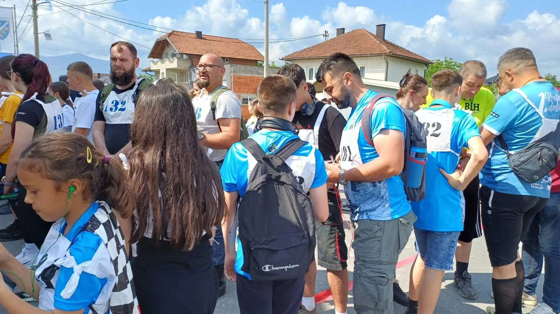 Grupa takmičara, uključujući djecu i odrasle, stoje u redu na startnoj liniji u sportskom takmičenju.