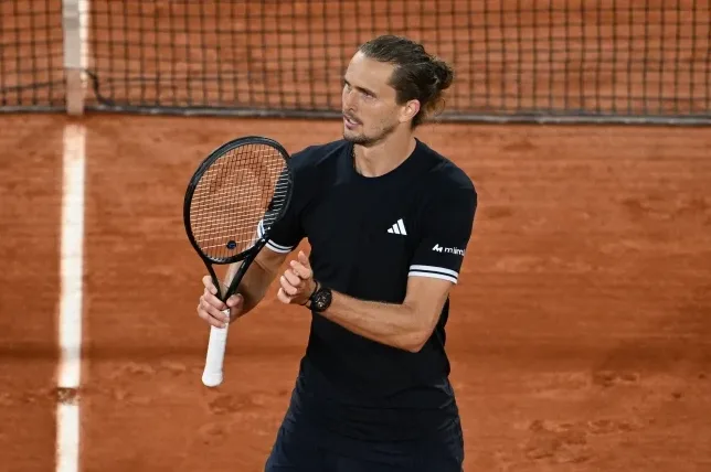 Muškarac sa podignutom kosom drži teniski reket i gleda lijevo, na teren za tenis napravljen od smeđe zemlje.