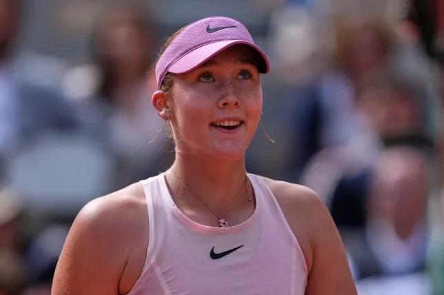 Mlada teniserka u roze Nike sportskom topu i roze viziru gleda gore, sa iskrenim osmijehom na licu, dok je u pozadini zamućena publika.
