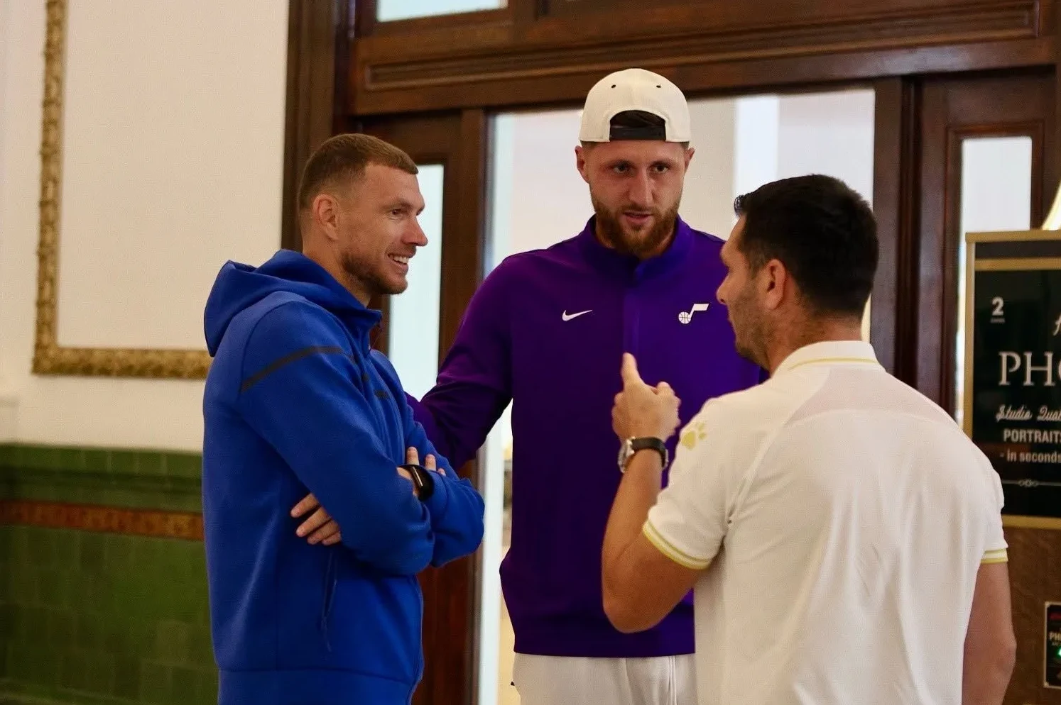 Troje muškaraca u sportskoj odjeći razgovara u zatvorenom prostoru.