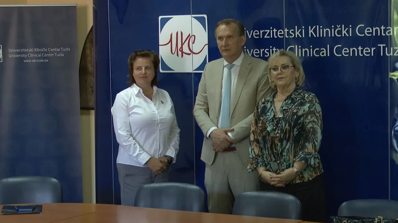 Tri osobe, dva muškarca i jedna žena, stoje ispred plave pozadine sa logom UKC Tuzla.