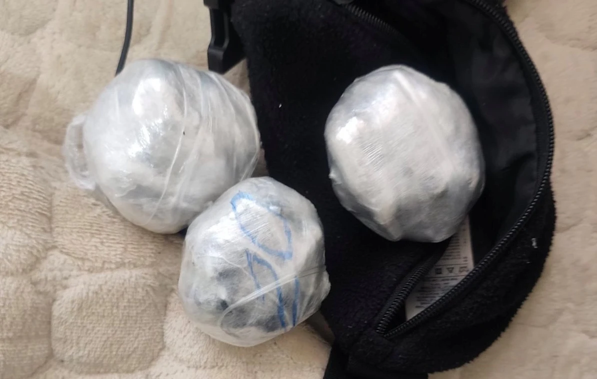 Tri okrugla paketa umotana u plastičnu foliju, od kojih jedan ima plave oznake, smještena su pored otvorene crne torbice.