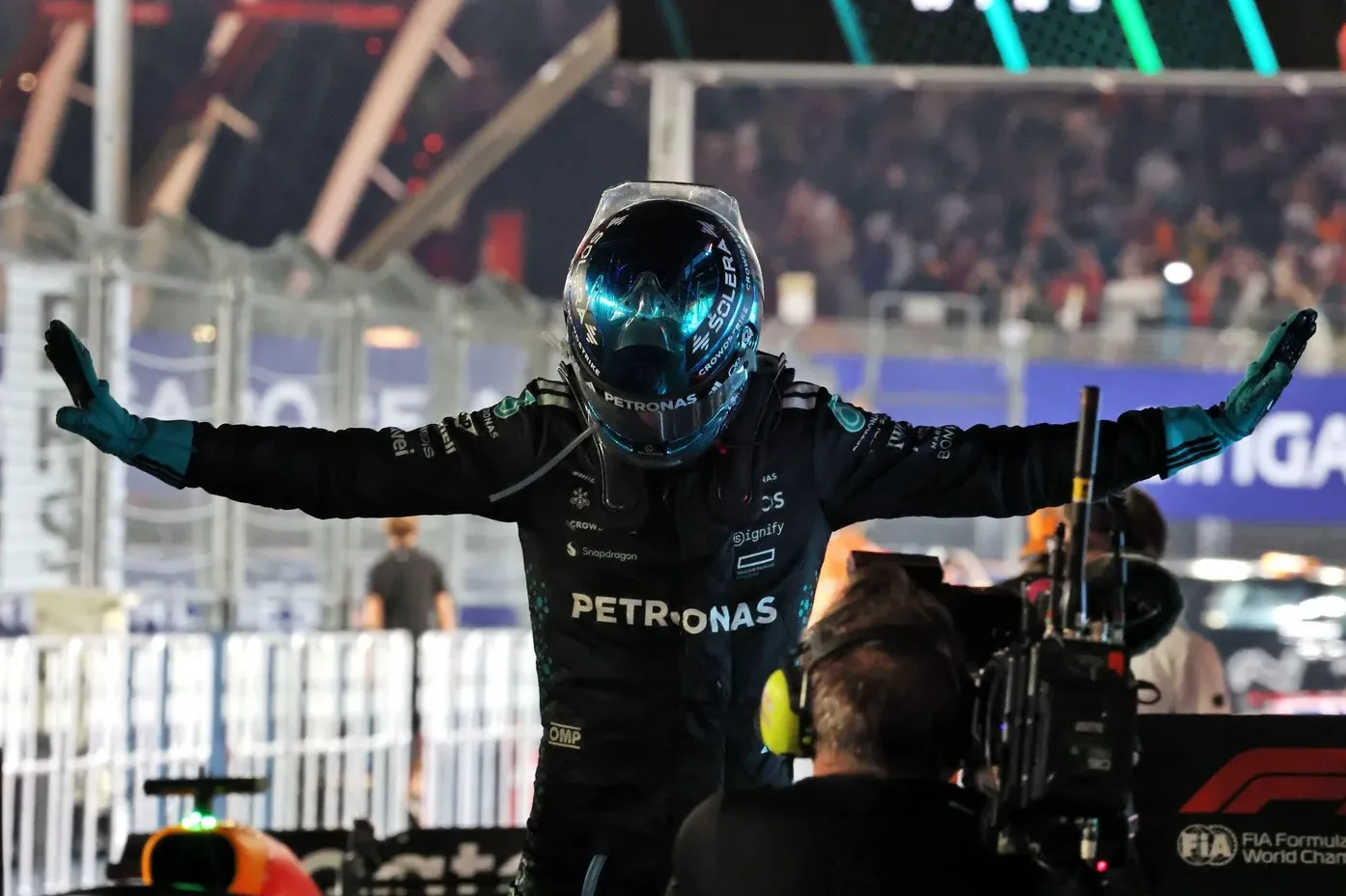 Vozač Formule 1 u Mercedesovom kombinezonu, sa kacigom, podignutih ruku u znak pobjede ili pozdrava.
