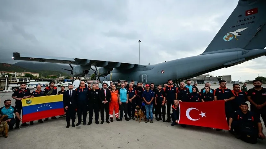 Grupa ljudi u uniformama, sa psom za potrage i spašavanje, pozira ispred velikog vojnog aviona turskog ratnog zrakoplovstva noseći zastave Venecuele i Turske.