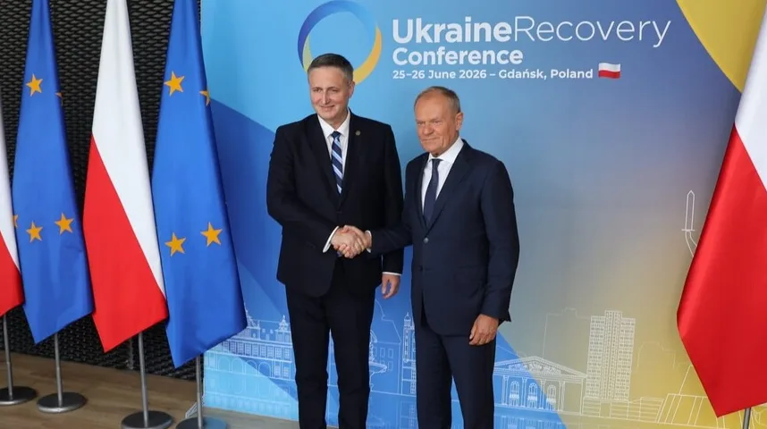 Dva muškarca u odijelima rukuju se ispred zastava Evropske unije i Poljske na konferenciji o obnovi Ukrajine.