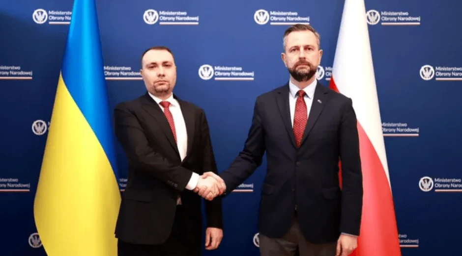 Dva muškarca u odijelima se rukuju ispred zastava Ukrajine i Poljske.