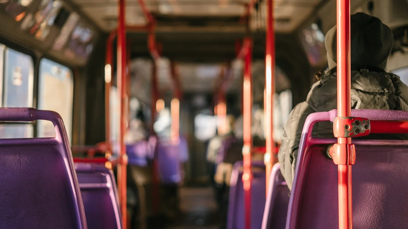 Pogled iznutra gradskog autobusa sa fokusom na ljubičasta sjedišta i crvene rukohvate u pozadini