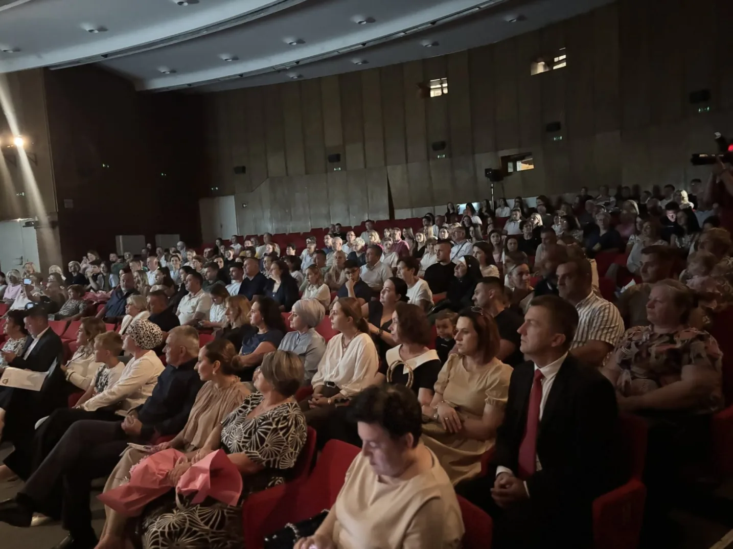 Publika sjedi u pozorišnoj sali, gleda prema pozornici.