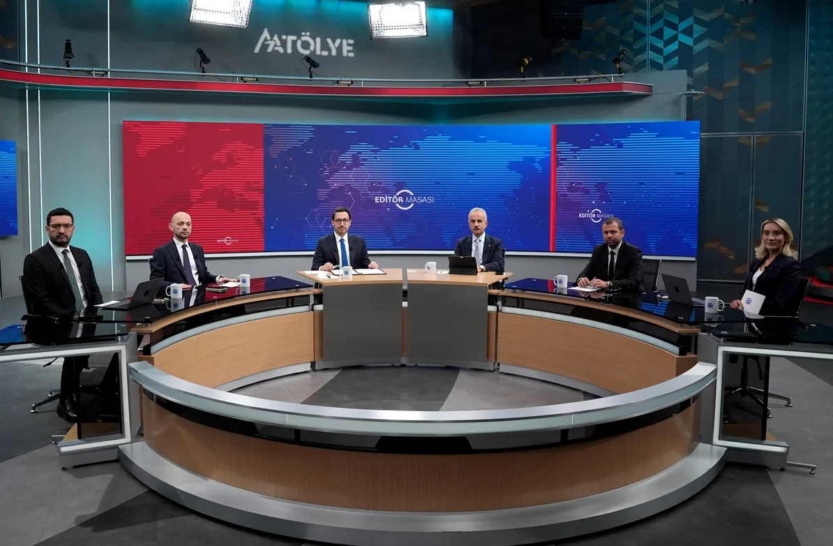 Grupa ljudi sjedi za okruglim stolom u modernom TV studiju.