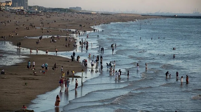 Puno ljudi uživa na plaži i u plitkoj morskoj vodi tokom sunčanog dana.