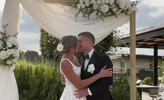 Mlada i mladoženja se ljube ispod svadbenog luka ukrašenog cvijećem.