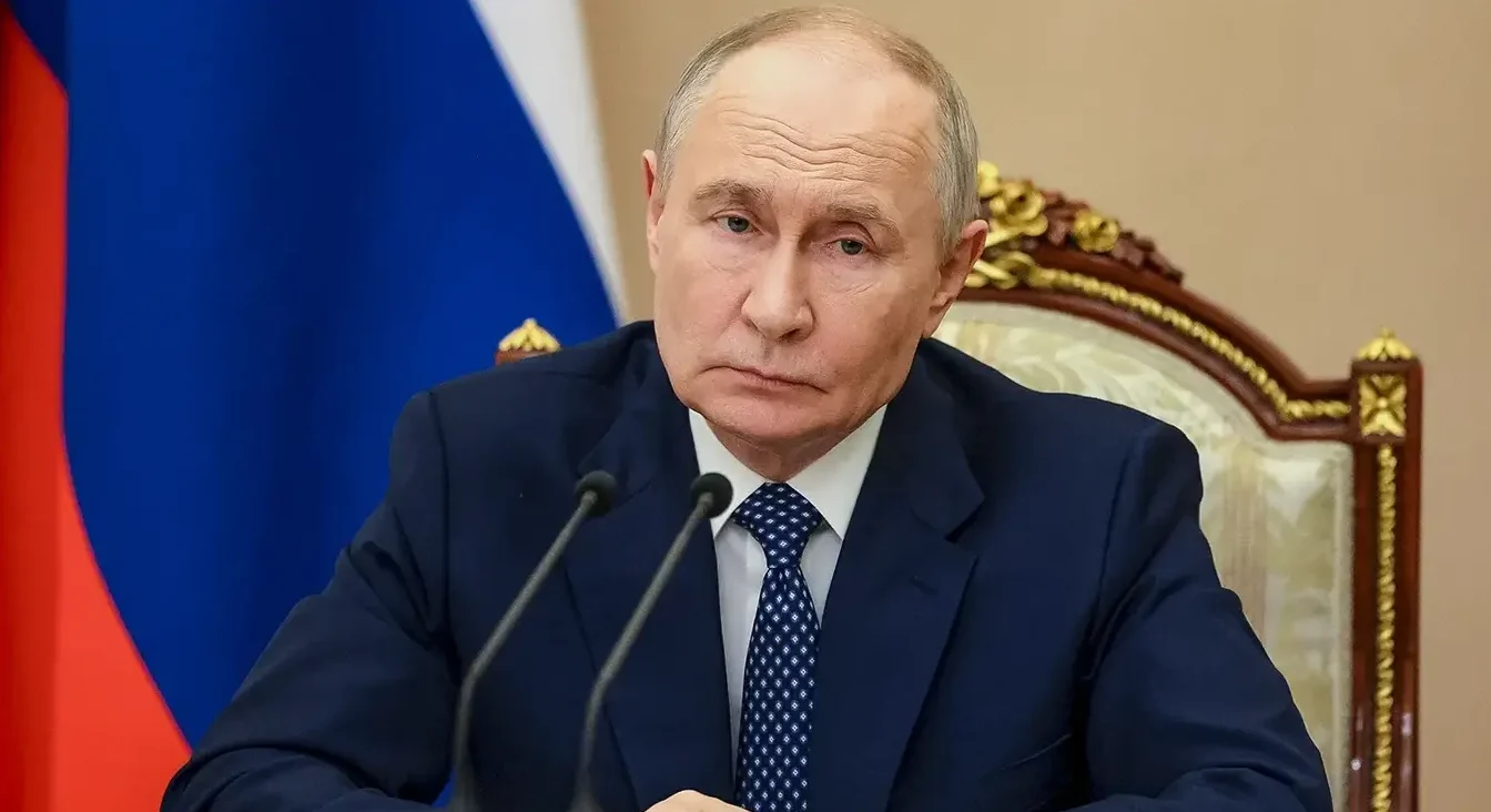 Vladimir Putin sjedi za stolom ispred ruske zastave.