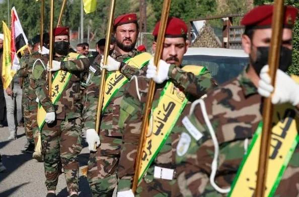 Muškarci u vojnim uniformama sa kamuflažnim uzorkom i crvenim beretkama na glavi, drže zlatne zastave i nose žute trake sa arapskim natpisima.