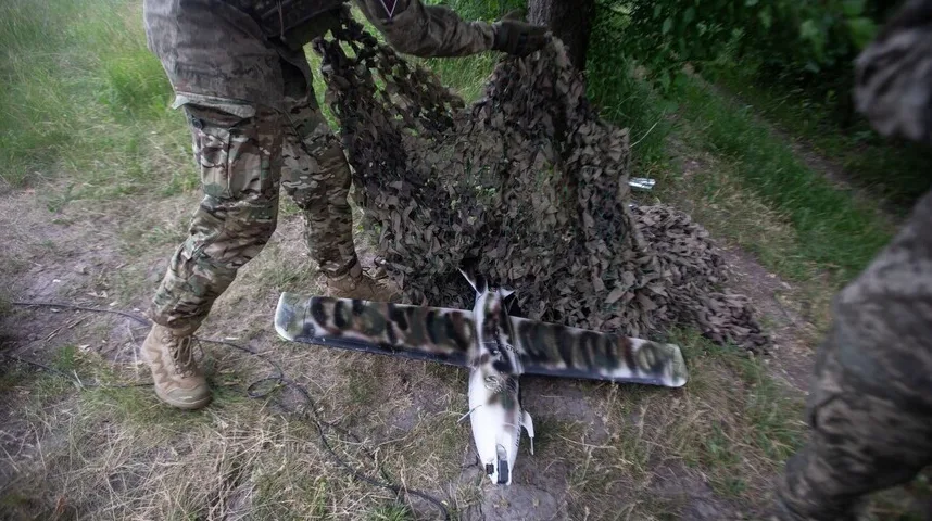 Vojnik u maskirnoj uniformi postavlja kamuflažnu mrežu preko ležećeg izvidjačkog drona.