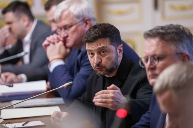 Predsjednik Ukrajine Volodimir Zelenski govori za govornicom na sastanku sa ljudima u odijelima.