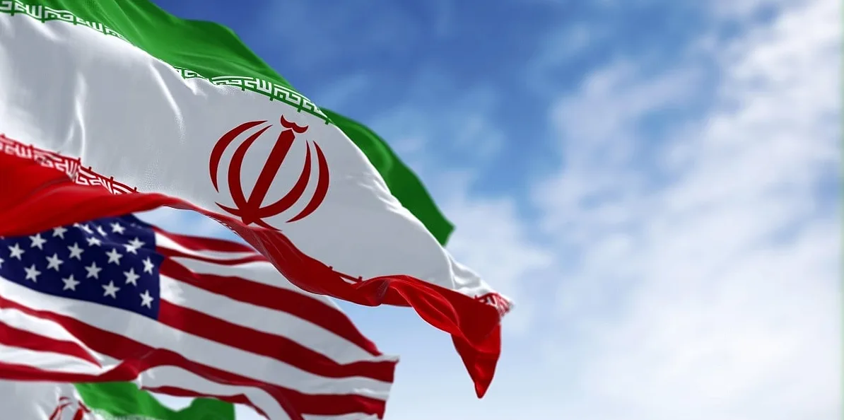 Zastava Islamske Republike Iran i zastava Sjedinjenih Američkih Država koje vijore na vjetru ispred plavog neba.