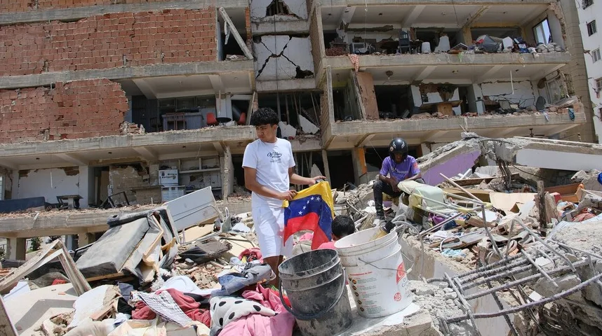 Mladić drži venezuelsku zastavu usred ruševina oštećene zgrade