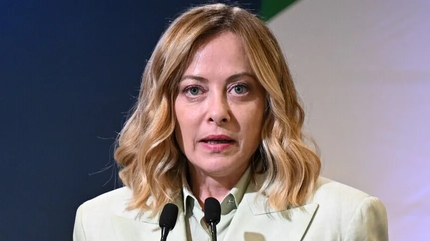 Portret žene sa plavom kosom koja govori iza postolja s dva mikrofona, odjevena u svijetlozeleni sako.