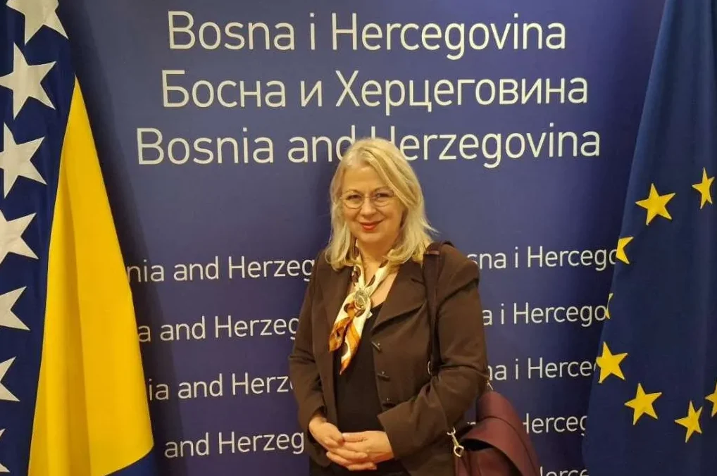 Portret žene sa plavom pozadinom sa natpisom "Bosna i Hercegovina" na tri jezika i zastavama Bosne i Hercegovine i Evropske unije.