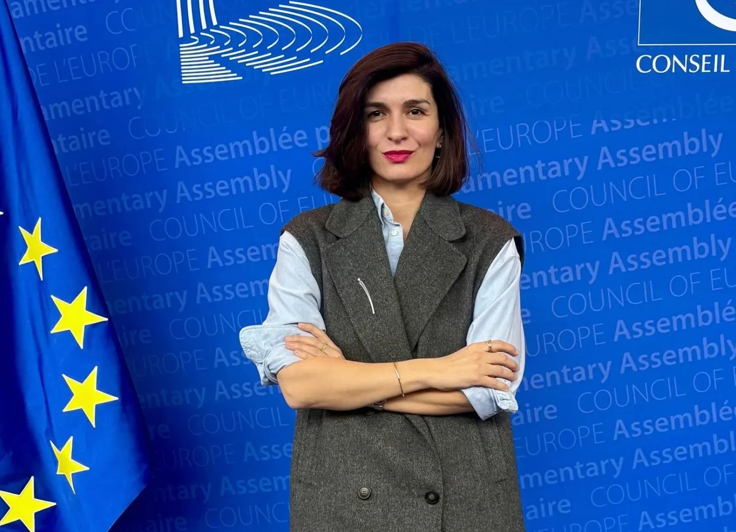 Portret žene koja stoji ispred plave pozadine sa zastavom Evropske unije i logom Savjeta Evrope.