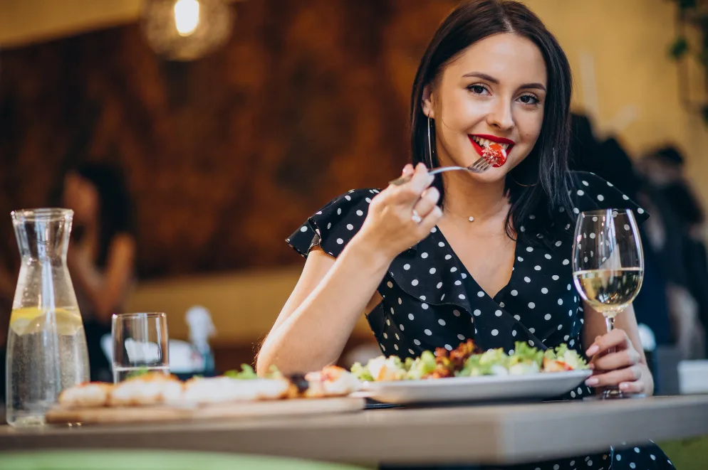 Mlada žena sa crvenim ružem jede salatu viljuškom u restoranu.