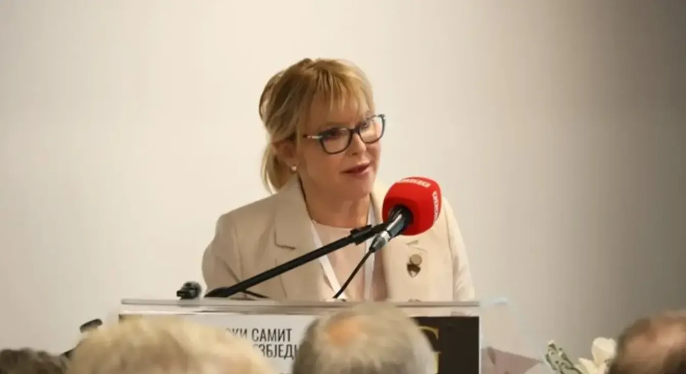 Žena sa plavom kosom i naočarima govori u mikrofon.