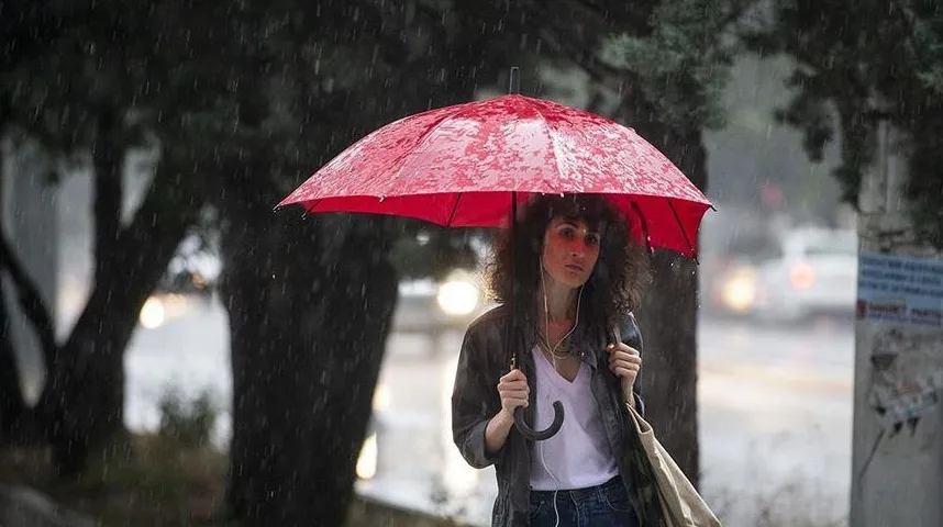 Žena sa smeđom kovrdžavom kosom nosi crveni kišobran dok stoji na ulici tokom kiše.