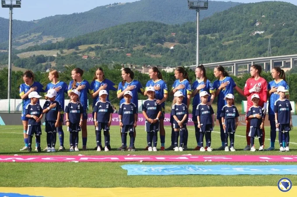 Ženska fudbalska reprezentacija Bosne i Hercegovine i dječaci iz omladinskih pogona stoje na terenu sa rukama na srcu, u čast himne.