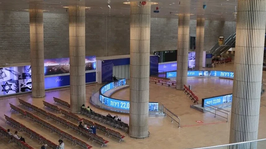 Unutrašnjost aerodroma Ben Gurion, Terminal 3, sa redovima sjedišta za putnike, velikim stubovima i LED ekranima.