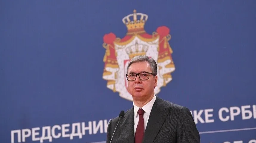 Aleksandar Vučić u odijelu i tamnoj kravati, sa naočarima, stoji ispred mikrofona. U pozadini se nalazi grb Srbije i natpis "PREDSJEDNIŠTVO SRBIJE".