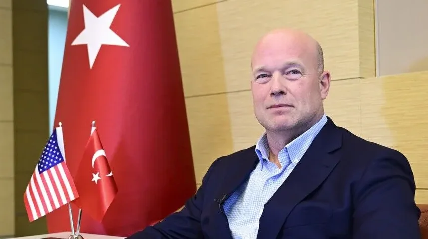Muškarac u tamnom odijelu sjedi ispred turske i američke zastave.