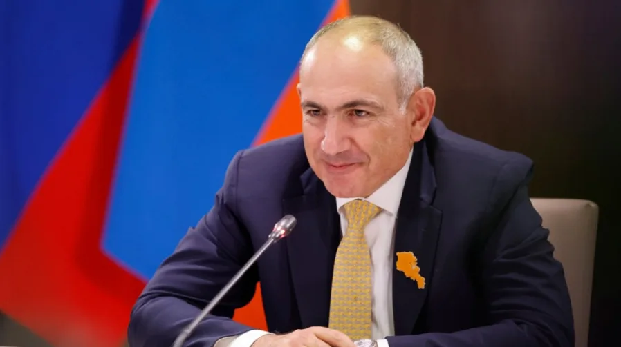 Političar u tamnom odijelu i žutoj kravati sa brošem u obliku mape Armenije.