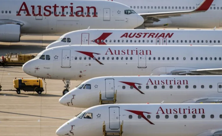 Više bijelih aviona Austrian Airlines parkiranih u redu na aerodromu, sa crvenim logotipom i natpisom "Austrian" na trupu.