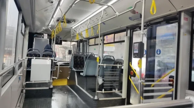 Unutrašnjost autobusa sa redovima sjedišta, rukohvatima i vratima.