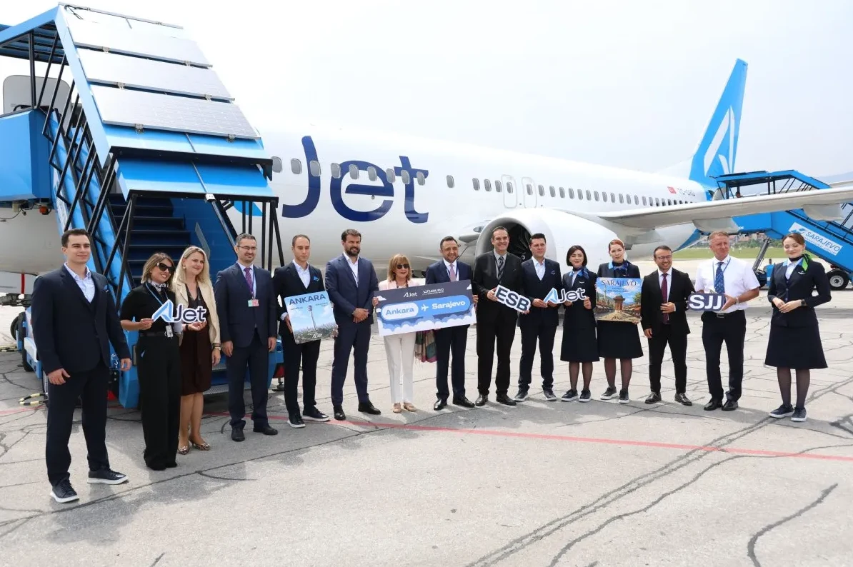 Grupa ljudi sa Ajet osobljem ispred aviona Ajet, držeći natpise sa oznakama destinacija