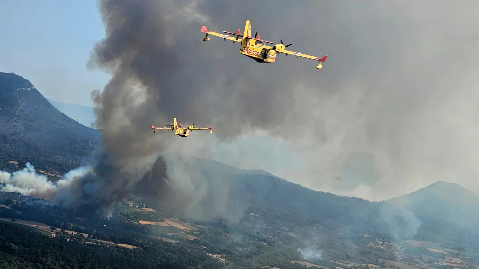 Kanaderi lete iznad gustog dima i plamena šumskog požara na planinskom području.