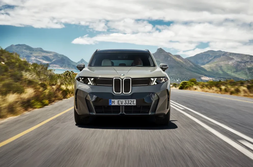 Prednji pogled na luksuzni električni automobil BMW i7 kako vozi krivudavim putem sa planinskim pejzažom u pozadini.