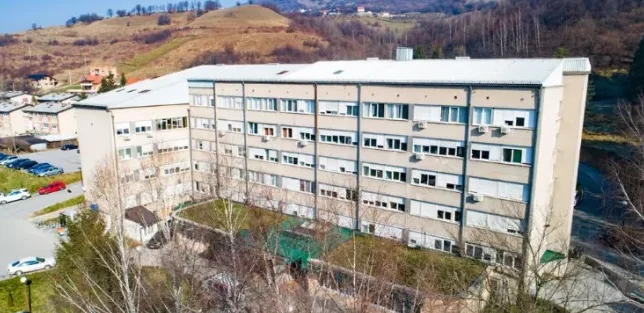 Izgled bolnice sa više spratova sa parkingom i stambenim zgradama u blizini.