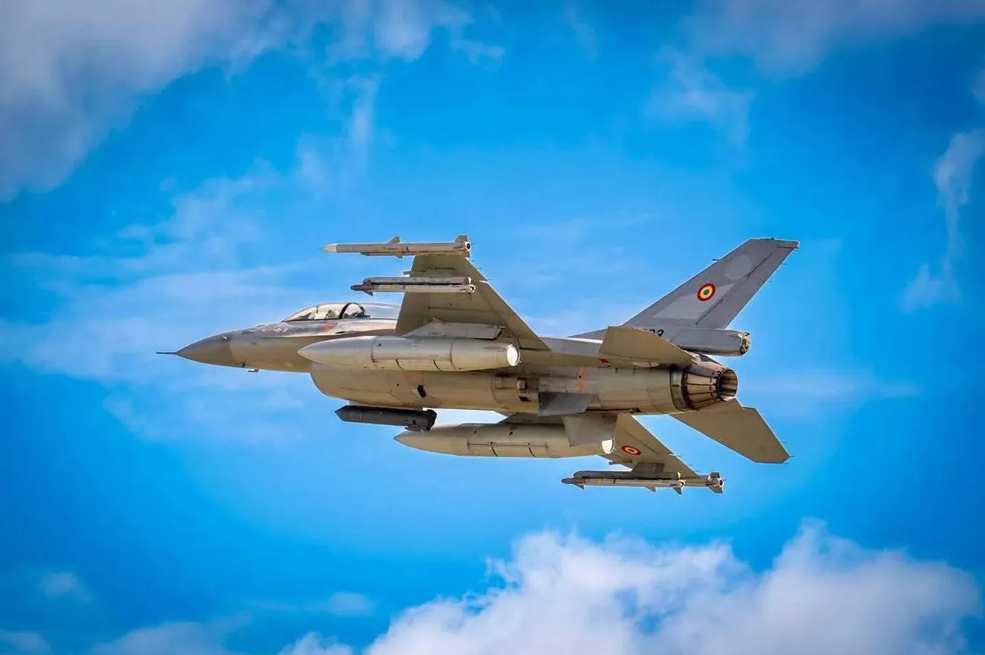 F-16 borbeni avion sa raketama naoružanja kako leti kroz plavo nebo sa oblacima.